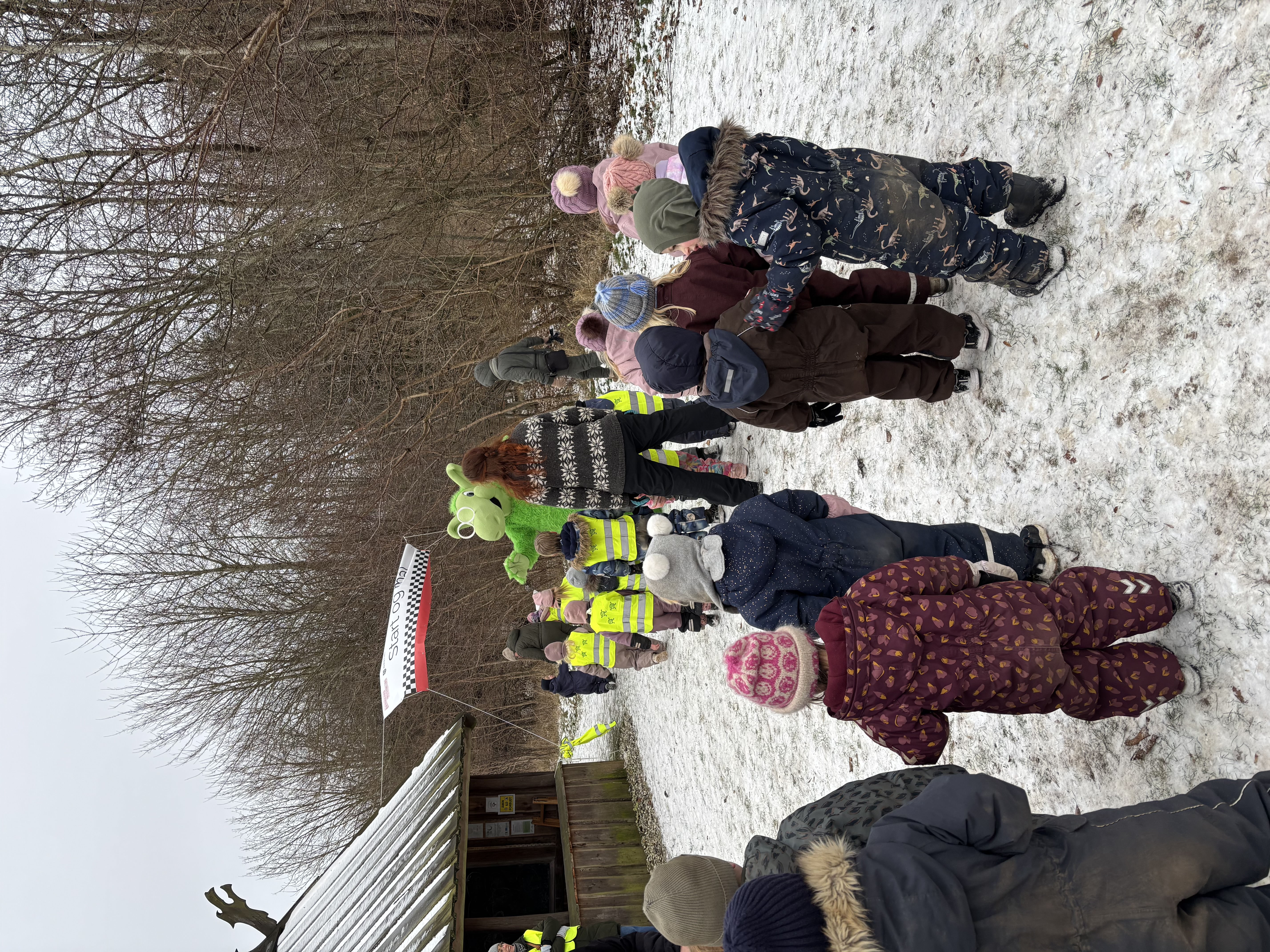 Den grønne drage Næssi tager imod gående børn ved et vikingelanghus i Folkeskoven i Tappernøje.